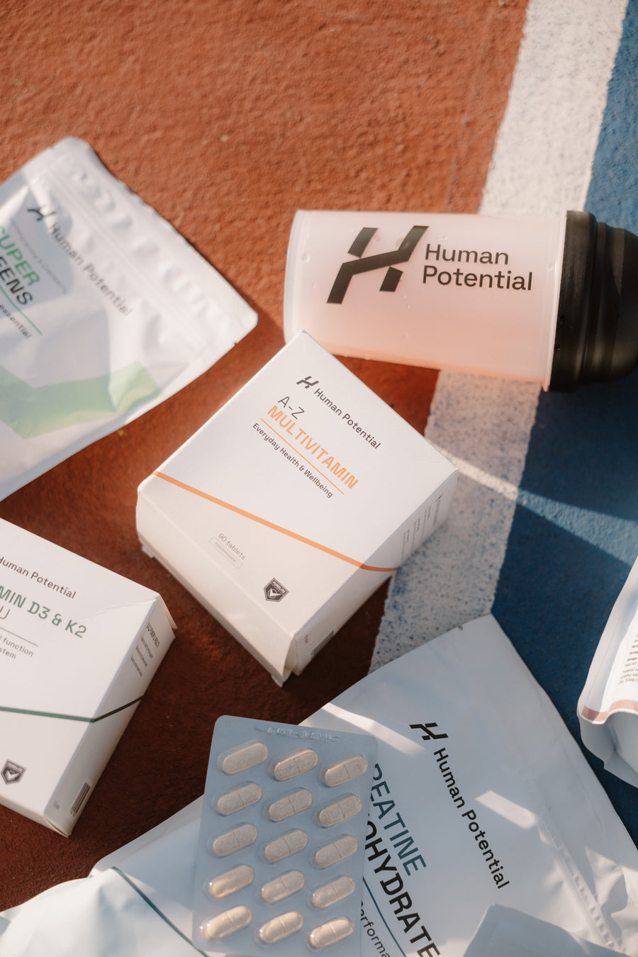 Several Human Potential branded supplement packets and a box arranged on a textured orange surface with painted white and blue lines in the background.